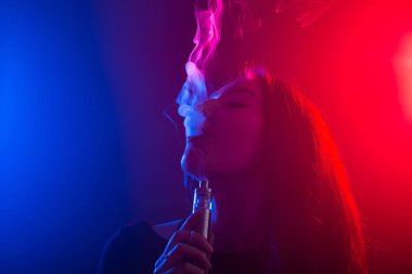 Neon ışık ve duman e-sigara veya vape koyu arka plan üzerinde genç kadın