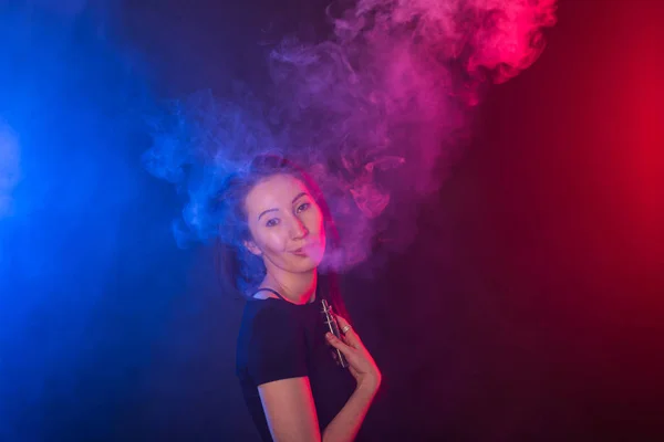 Mujer joven en luz de neón y humo de cigarrillos electrónicos o vapor sobre fondo oscuro — Foto de Stock