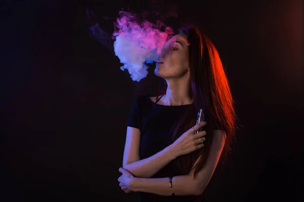 Portrait of young woman in neon red and blue smoke with vape or e-cigarettes — Stock Photo, Image
