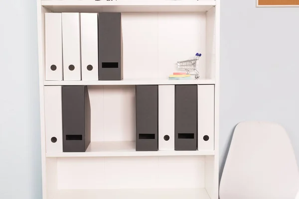 Interni, concetto di ufficio - uno scaffale bianco con una quantità di file e piccolo carrello della spesa giocattolo — Foto Stock