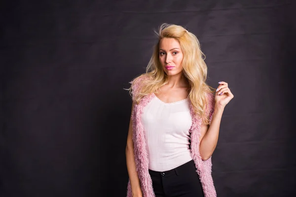 Modelagem, moda, pessoas concepto- jovem loira séria em casaco rosa sobre o fundo preto com espaço de cópia — Fotografia de Stock
