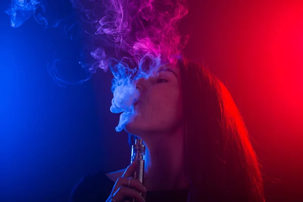 Retrato de menina na fumaça de néon colorido com vape ou cigarro eletrônico . — Fotografia de Stock