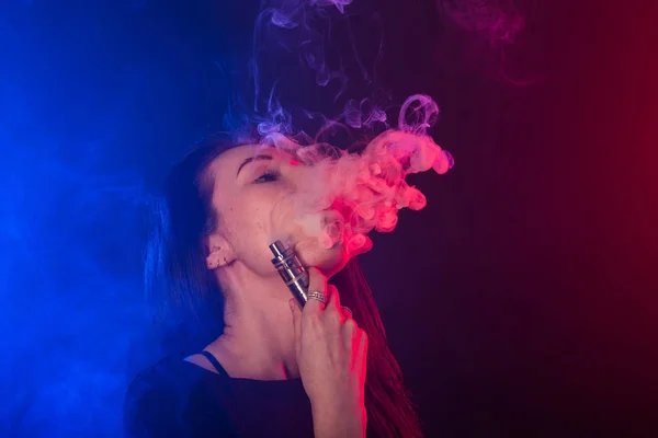 Retrato de mulher jovem em néon fumaça vermelha e azul com vape ou e-cigarros . — Fotografia de Stock