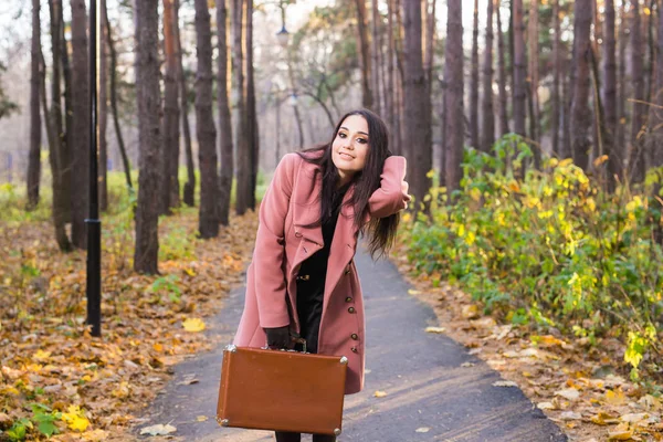 Otoño, temporada y concepto de personas - mujer en abrigo rosa con estuche marrón de pie en el parque de otoño sobre el fondo de la naturaleza — Foto de Stock