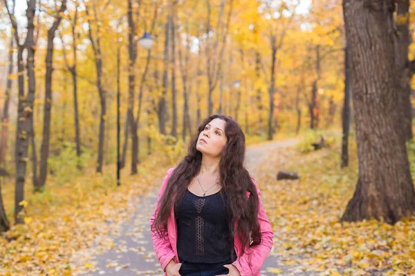 Herfst, de natuur en de mensen concept - jonge vrouw kijken naar de hemel in de herfst park. Ze wordt in roze jasje — Stockfoto
