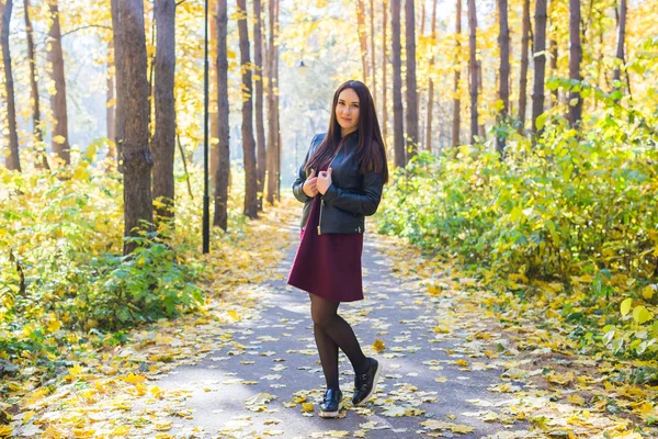 Herbst, Natur, Menschen - junge schöne Frau spaziert im Herbstpark in rotem Kleid und schwarzer Jacke — Stockfoto