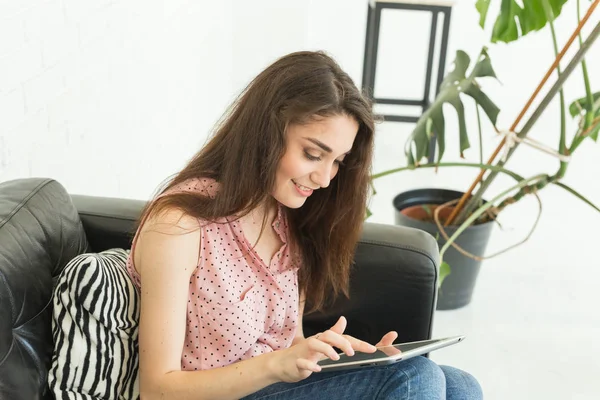 Tecnologie, concetto di persone - giovane donna seduta sul divano a guardare il tablet o navigare in rete e sorridere — Foto Stock