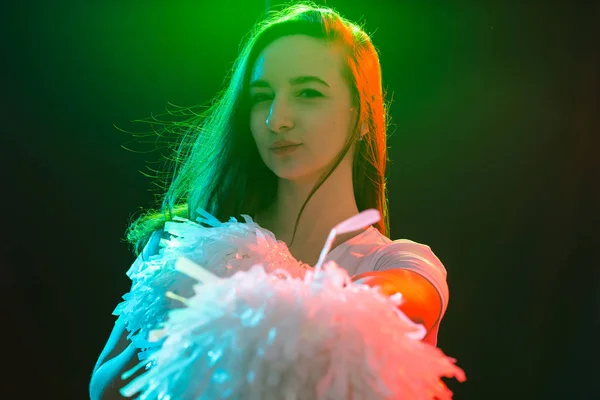 Dançando, esporte, bonito e conceito de pessoas - jovem menina líder de torcida na escuridão mostrar pom poms e sorrir — Fotografia de Stock