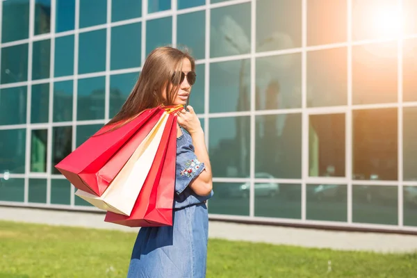 Einkauf, Rabatt- und Personenkonzept - Porträt einer jungen Frau im Kleid, die mit bunten Einkaufstaschen spaziert — Stockfoto