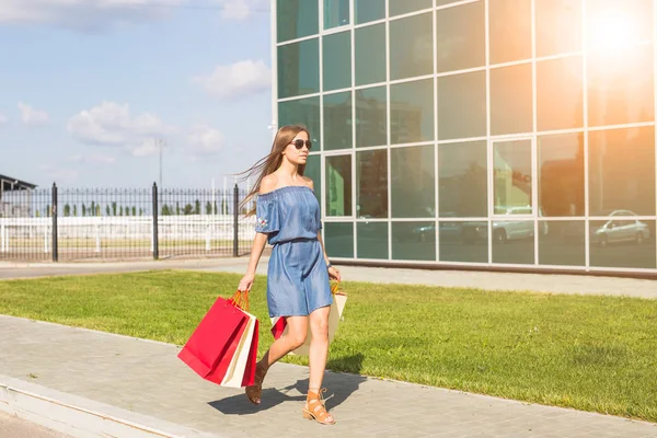 Έννοια του καταναλωτισμού, πώληση και άτομα - νεαρή γυναίκα, που μεταφέρουν τσάντες για ψώνια, ενώ το περπάτημα κατά μήκος του δρόμου — Φωτογραφία Αρχείου