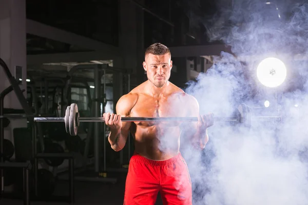 Bodybuilder, der die Übungen mit der Langhantel macht. kräftiges Männchen mit nacktem Oberkörper auf dunklem Hintergrund. Stärke und Motivation. — Stockfoto