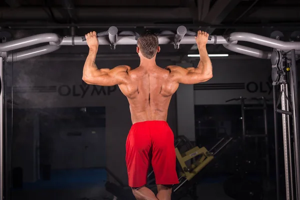 stock image Strong young man doing pull up exercise on horizontal bar in gym