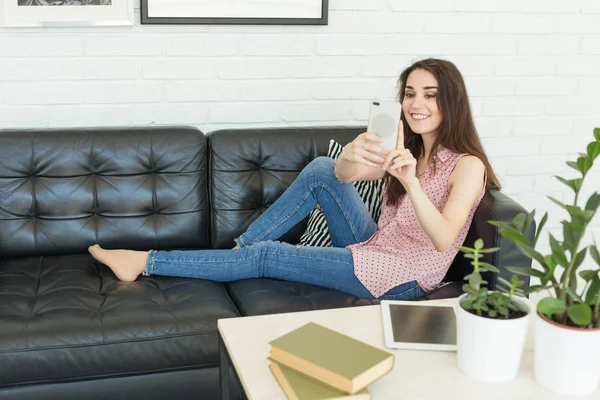 Giovane donna che prende selfie mentre si siede sul divano a casa — Foto Stock