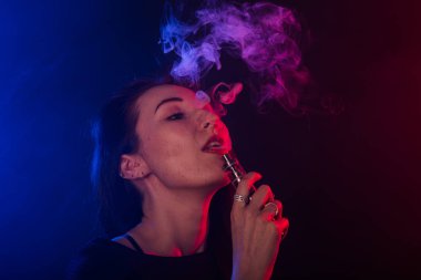 Neon ışık ve duman e-sigara veya vape koyu arka plan üzerinde genç kadın