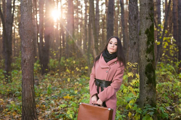 Concepto de moda, temporada y la gente - mujer joven feliz se va en un viaje con maleta retro en un fondo de follaje de otoño — Foto de Stock