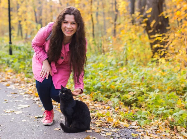 Menschen, Haustierbesitzer und Saisonkonzept - junge Frau und eine schwarze Katze im Herbstpark — Stockfoto