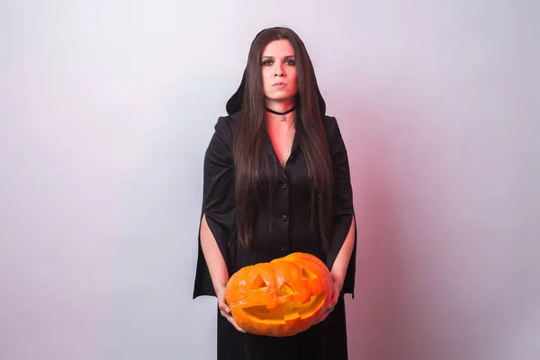 Young woman in Halloween witch costume in studio with yellow pumpkin on white background with copy space — Stock Photo, Image