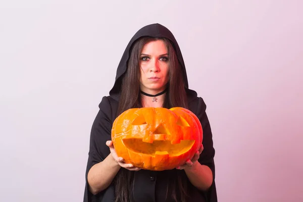 Jonge vrouw in Halloween heks kostuum in studio met gele pompoen. — Stockfoto