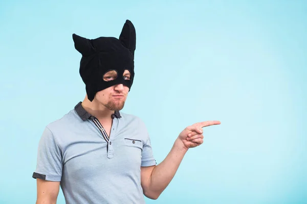 Mann mit schwarzer Maske zeigt auf blauem Hintergrund mit Kopierraum. Anonyme soziale Maskierung. halloween — Stockfoto