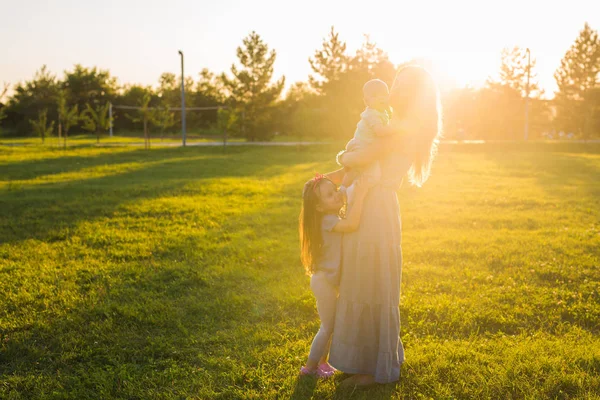 Vacker kvinna med dotter och baby son på grönt gräs fält. Mamma med två små barn kramas utomhus. Lycklig familj koncept — Stockfoto