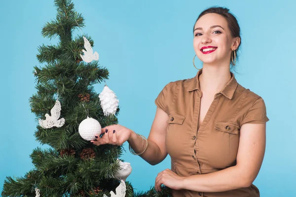 People, holidays and celebrations concept - young woman with christmas tree on blue background