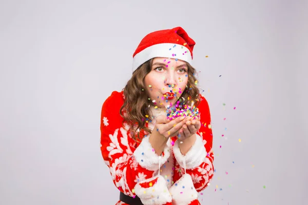 Hermosa chica en traje de Santas dando la bienvenida al nuevo año 2019 soplando confeti a la cámara. Celebración de Año Nuevo y concepto de fiesta — Foto de Stock