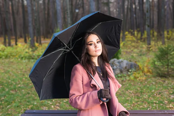 Otoño, temporada y concepto de personas - mujer joven sentada en un banco en el parque en otoño con paraguas —  Fotos de Stock