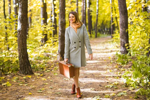 Natureza, estação e conceito de pessoas - jovem mulher com mala sorrindo no parque de outono — Fotografia de Stock