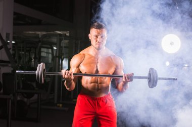 Siyah arka planda ağırlık kaldıran kaslı bir gencin yakın çekimi.