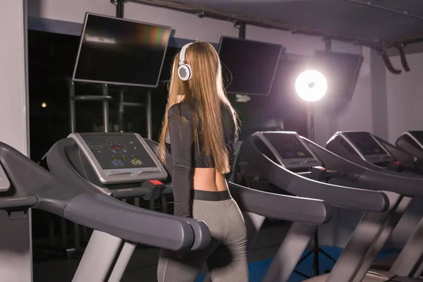 Fitness woman running on treadmill. Girl with muscular legs in gym