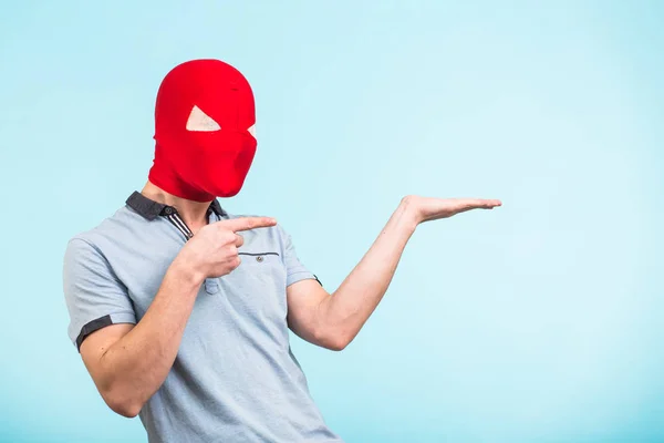 Mannen bär röd mask pekar på blå bakgrund med kopia utrymme. Anonym sociala maskering koncept. Halloween — Stockfoto