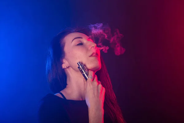 Mujer joven en camiseta negra vapeando en luz de neón roja y azul —  Fotos de Stock