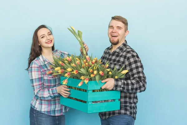 Glücklicher Mann und Frau Floristen halten Schachtel mit Tulpen und lachen auf blauem Hintergrund — Stockfoto