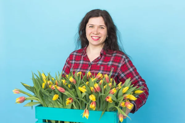 Joyeux jeune femme tenant une boîte de tulipes sur fond bleu — Photo