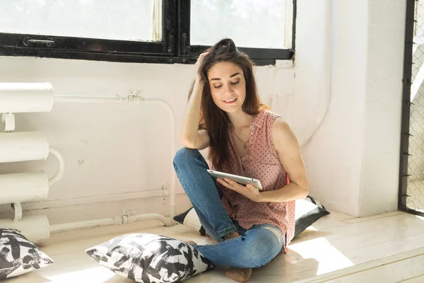 Tecnologia e concetto di persone - Giovane bella donna seduta sul davanzale di legno con tablet e cuscini — Foto Stock