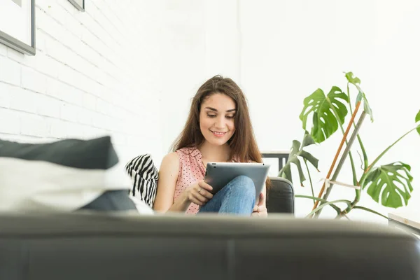 Technologies, communication, concept de personnes - la jeune femme est assise sur le canapé et bavarde dans une tablette et sourit — Photo