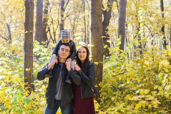 Família, outono, conceito de pessoas - jovem família caminhando no parque no dia de outono, abraçando e sorrindo — Fotografia de Stock