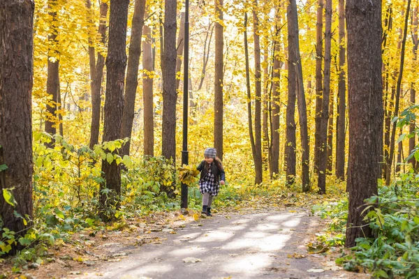 Herfst, geluk en mensen concept - kind loopt door herfst park met gele bladeren in haar handen — Stockfoto