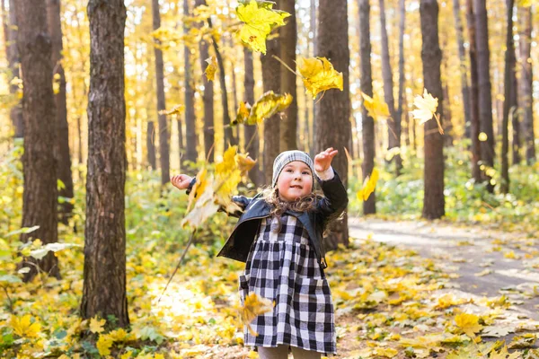 Otoño, estaciones y concepto de niños - niña feliz riendo y jugando con hojas caídas en el parque —  Fotos de Stock