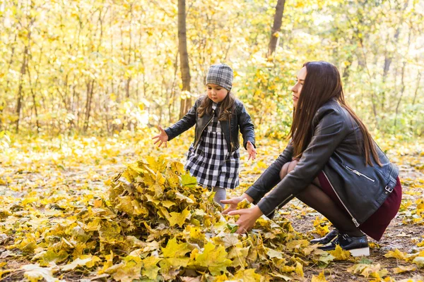 Fall, family, people concept - mother and daughter having fun in the autumn park in leaves