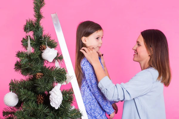 Helgdagar, familj och jul koncept - mor och dotter dekorera julgran på rosa bakgrund — Stockfoto