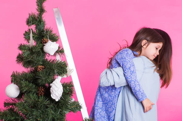Ung mamma och hennes dotter med julgran på rosa bakgrund — Stockfoto