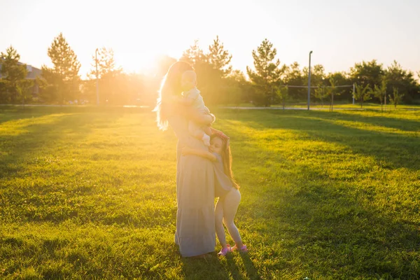 Mulher bonita com filha e filho bebê no campo de grama verde. Mãe com dois filhos pequenos abraçando ao ar livre. Conceito de família feliz — Fotografia de Stock