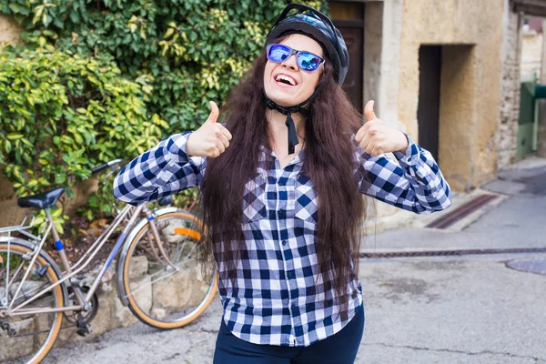 헬멧과 선글라스에 쾌활 한 여자 축구 표시 엄지손가락 배경 자전거 및 거리에 — 스톡 사진
