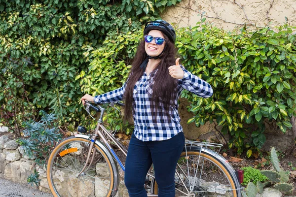 헬멧과 선글라스에 젊은 여자, 보여주는 셔츠를 엄지 누르고 자전거 — 스톡 사진