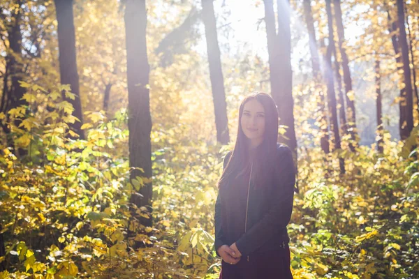 Herfst, de natuur en de mensen concept - jonge brunette vrouw in leren jas wandelen in het park — Stockfoto