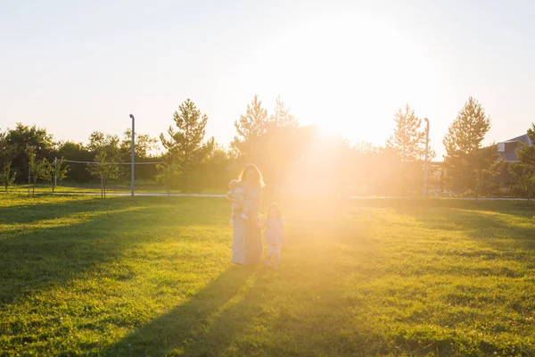 Hermosa mujer con hija e hijo bebé en el campo de hierba verde. Madre con dos niños pequeños caminando al aire libre. Concepto de familia feliz — Foto de Stock