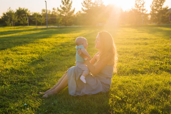晴れた日に草原の上の男の子と若い女性。夏の日没の幸せな家族。赤ちゃんと母親. — ストック写真