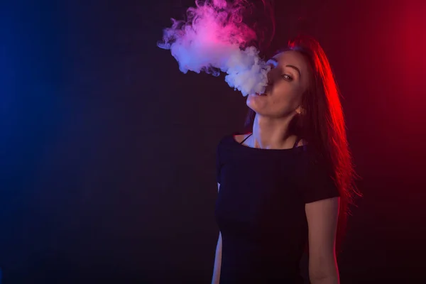 Retrato de mujer asiática fumando vapor o cigarrillo electrónico en luz de neón en fondo negro . — Foto de Stock