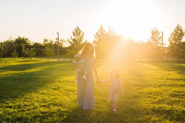 Красива жінка з дочкою і маленьким сином на осінньому полі. Мама з двома маленькими дітьми обіймається на відкритому повітрі. Щаслива сімейна концепція — стокове фото